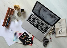 Top view of a creative workspace with a laptop, sketch supplies, and color palette.